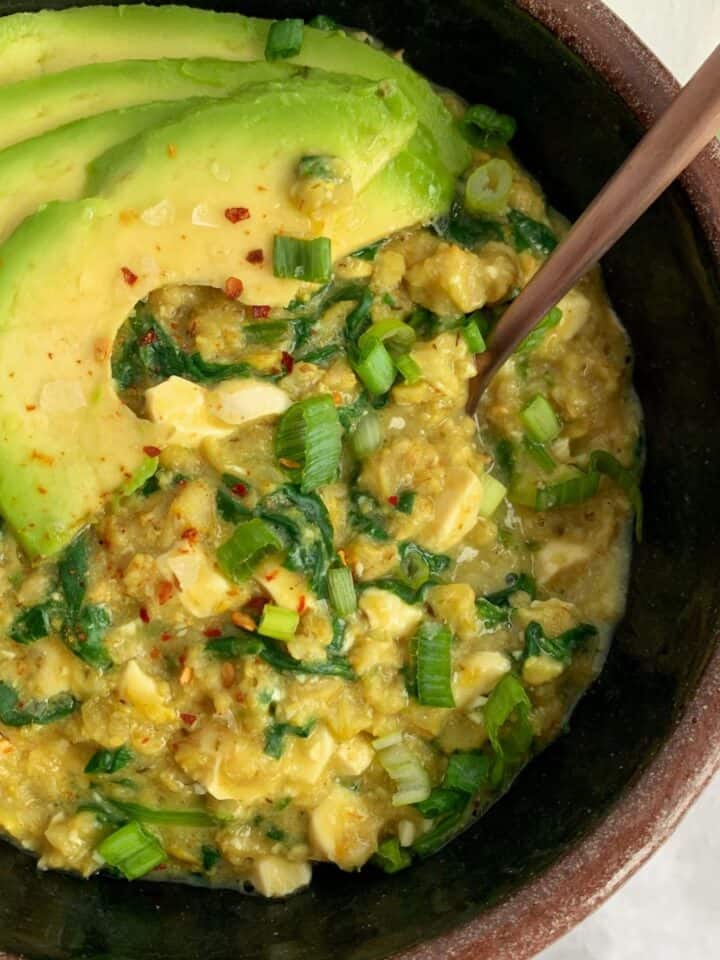 savory oatmeal with spinach and avocado in a bowl with a spoon.