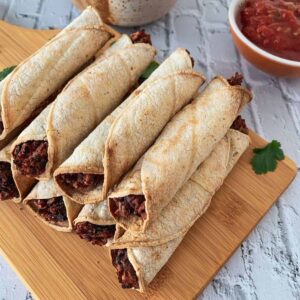 black bean air fryer taquitos on a wood cutting board and white tile background
