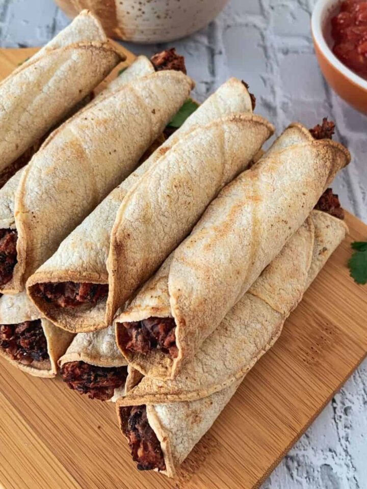 black bean air fryer taquitos on a wood cutting board and white tile background