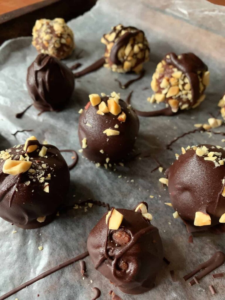 Chocolate Peanut Butter Truffles on wax paper with chopped peanuts and chocolate drizzle