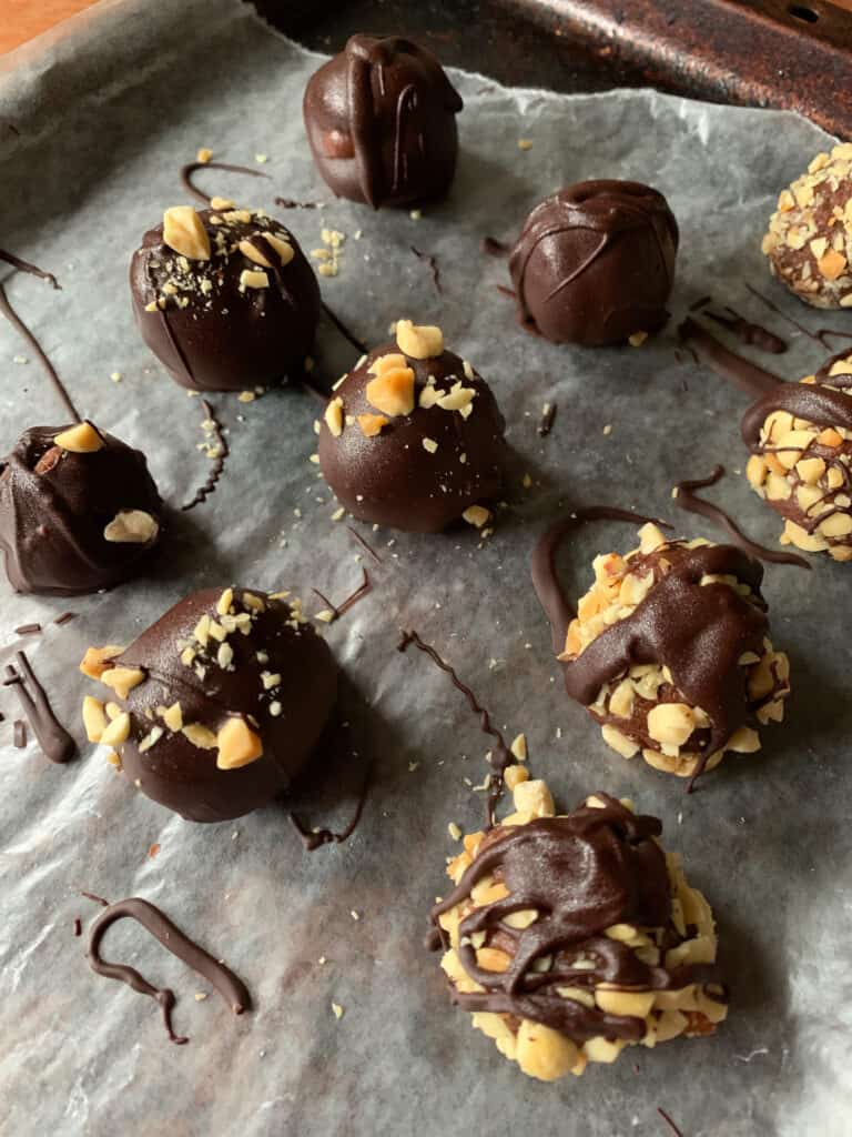Chocolate Peanut Butter Truffles on wax paper with chopped peanuts and chocolate drizzle