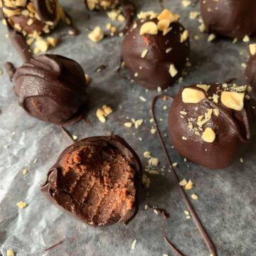 Chocolate Peanut Butter Truffles with a bite taken out of one on wax paper with chopped peanuts and chocolate drizzle