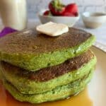 green blender pancakes topped with butter and syrup on a white plate with berries and milk in the background