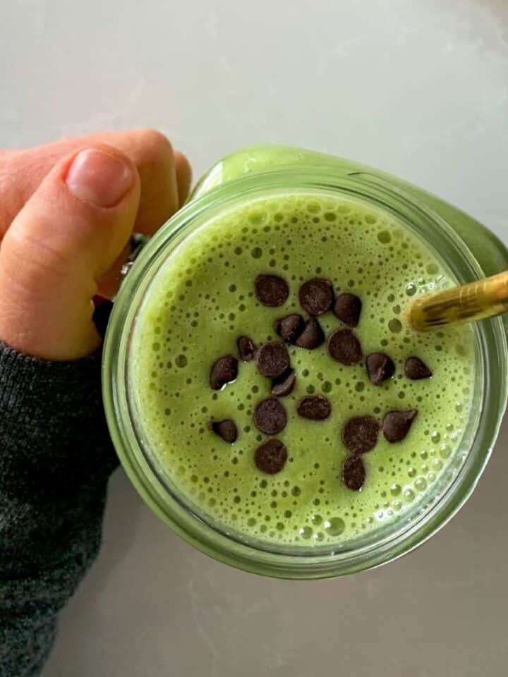 green shamrock shake in a mason jar topped with mini chocolate chips held in hand