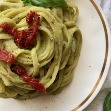creamy lemon basil fettucine on a white and gold plate with a white background and basil and sundried tomato