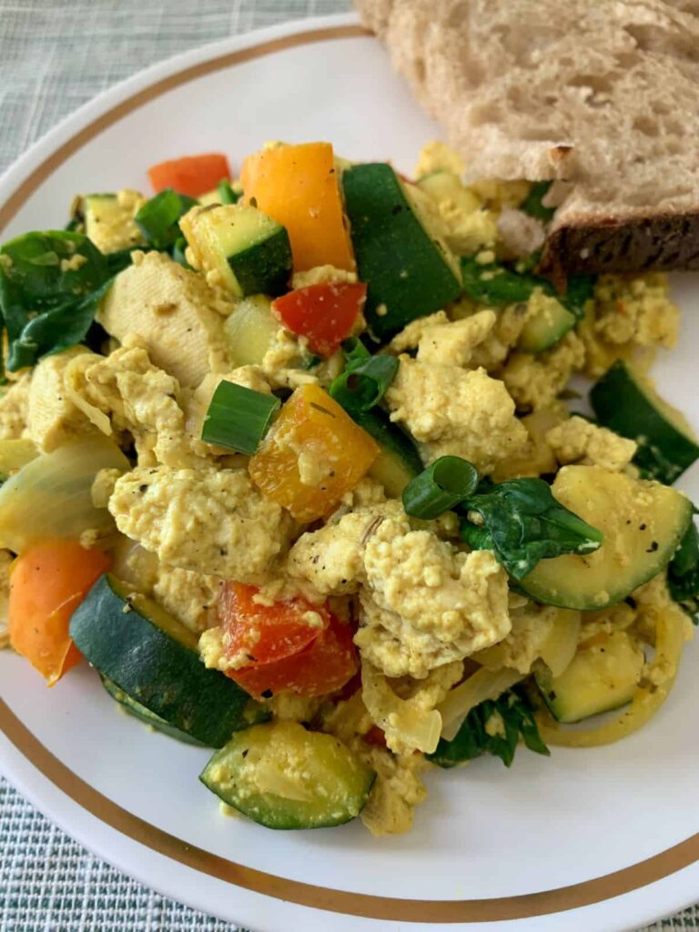 tofu scramble with veggies on a white plate with gold rim and sourdough toast