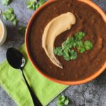 black bean soup with cilantro and cashew cream topping in an orange bowl with lime green napkin