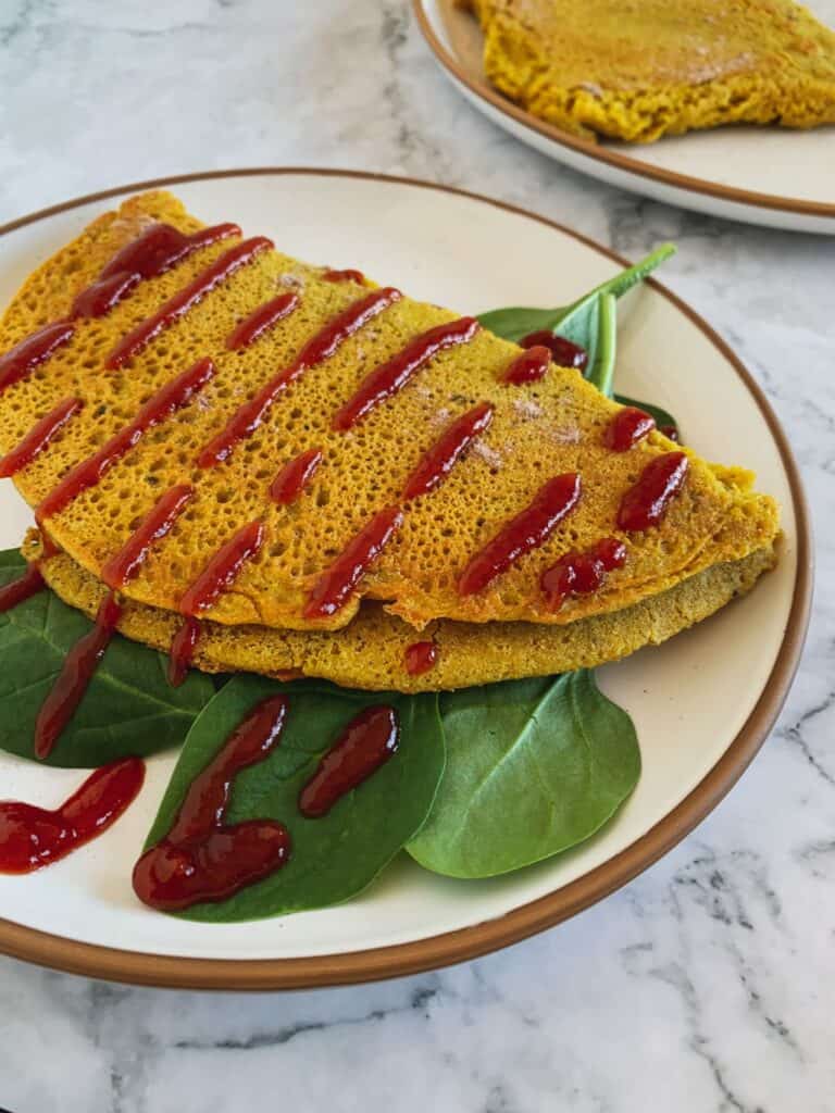 chickpea egg omelet with ketchup and spinach on a white plate and marble background