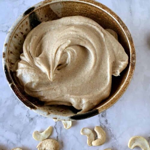 cashew date frosting in a brown ceramic bowl with white background and cashews