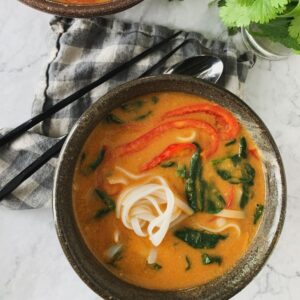 curried red lentil noodle soup in a ceramic bowl with black chopsticks and a grey white napkin
