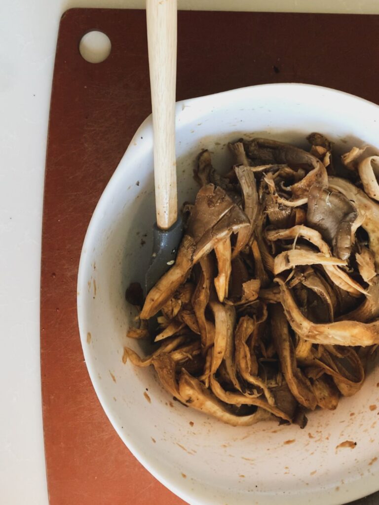 shredded oyster mushrooms in a large white mixing bowl with marinade