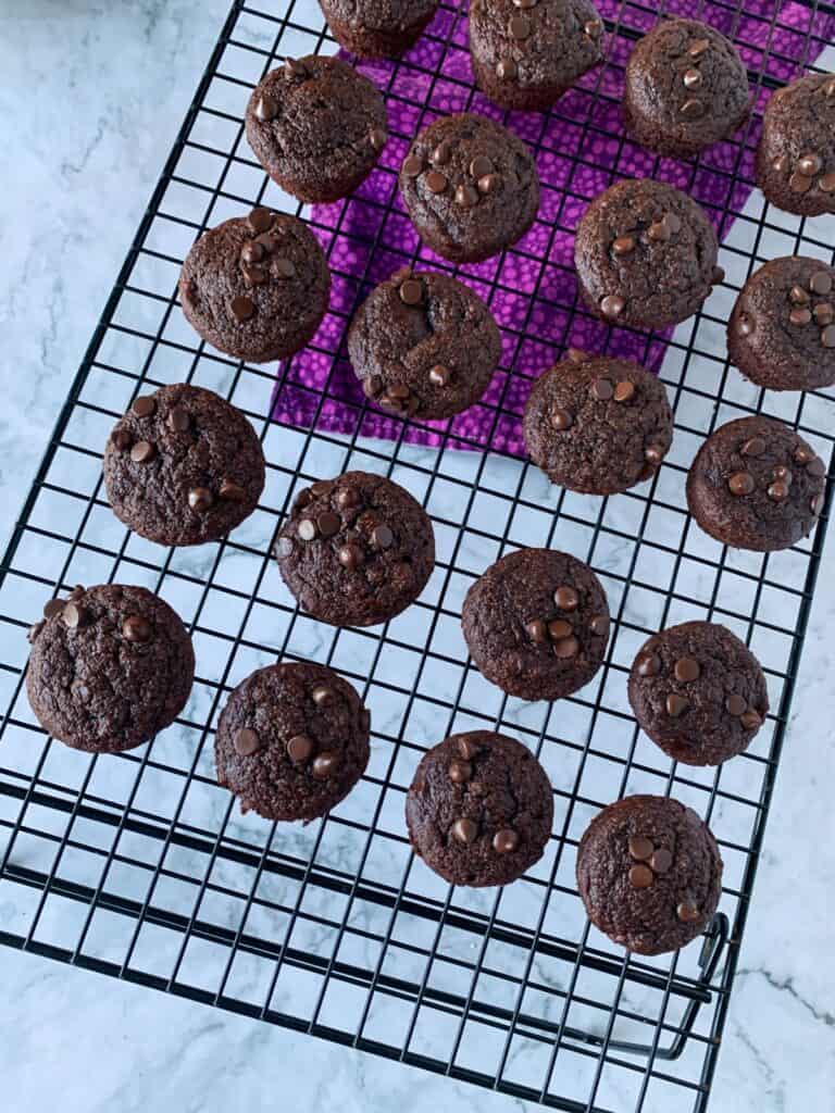 vegan chocolate banana bread mini muffins cooling on a black wire rack with white background and purple napkin