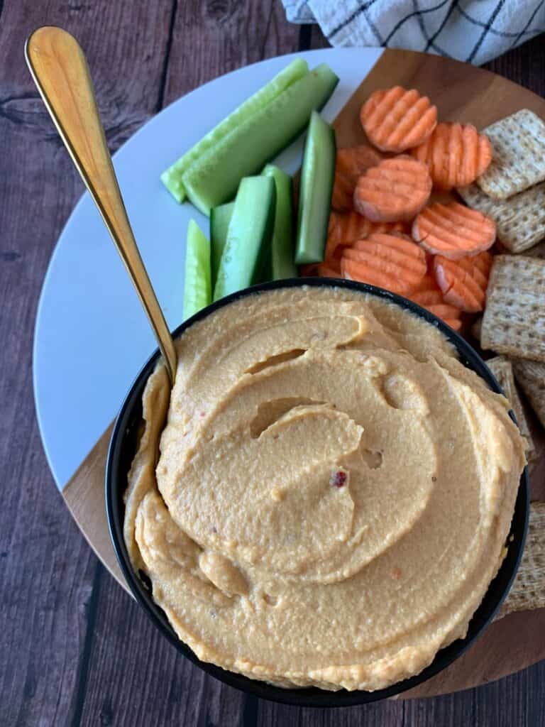 smooth sweet potato hummus in a black bowl served on a wooden background with cut cucumber, carrot and crackers
