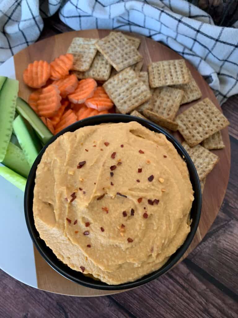 Sweet potato hummus in a bowl with a platter of cut cucumber, carrot and crackers
