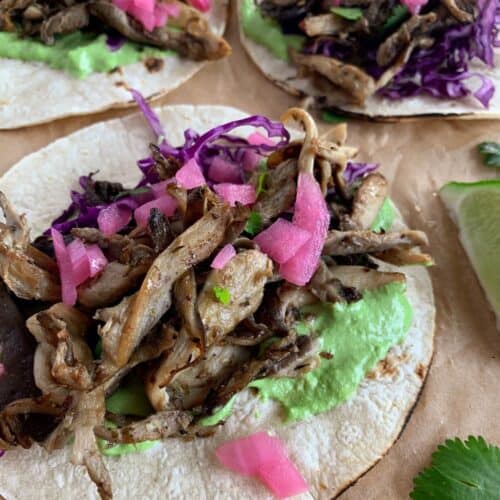 close up of oyster mushroom taco, toasted corn tortilla with cilantro crema, mushrooms, pickled onions and red cabbage