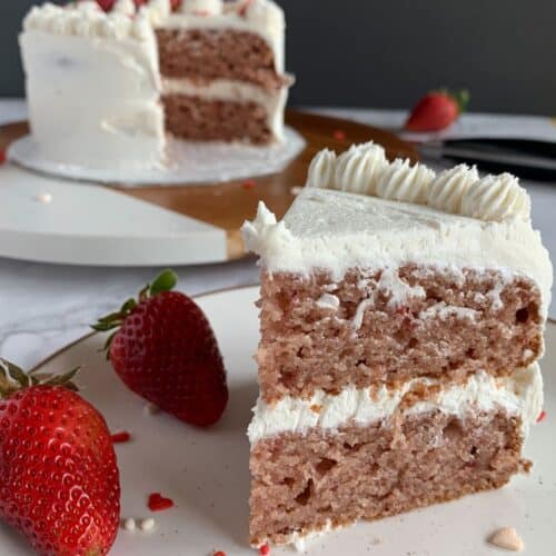 slice of vegan strawberry cake with vanilla buttercream frosting on a white plate