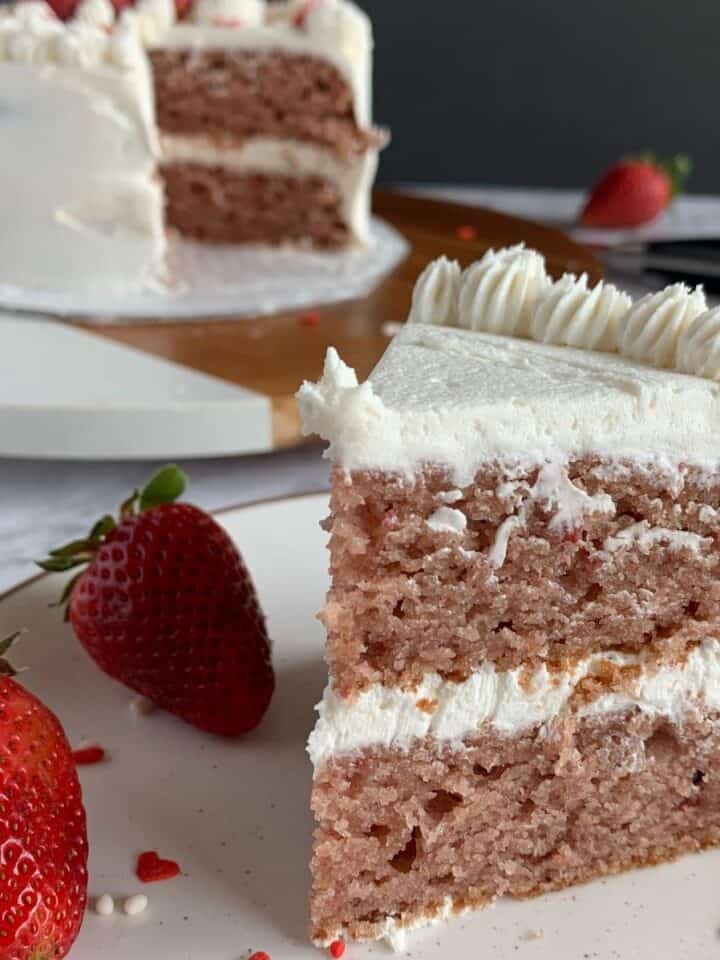 slice of vegan strawberry cake with vanilla buttercream frosting on a white plate