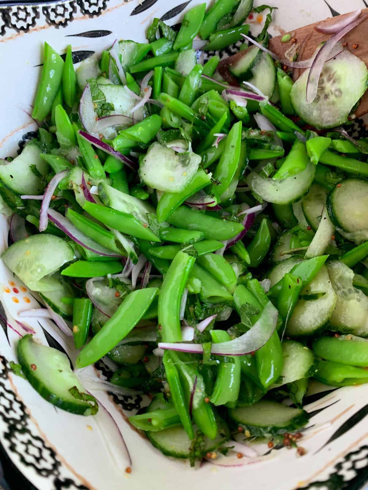 sugar snap pea salad mixed and ready to serve in a white and black bowl