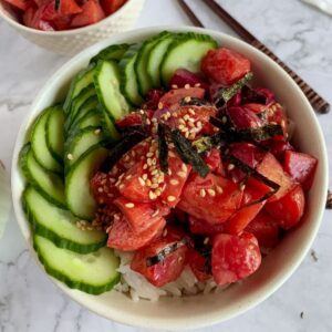vegan beet poke in a white ceramic bowl over rice with cucumber & sesame seeds