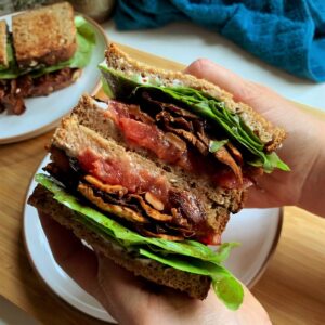 vegan blt sandwich cut in half and held in hands