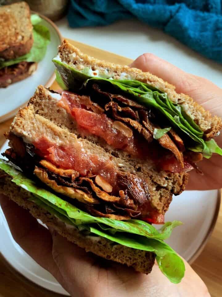 vegan blt sandwich cut in half and held in hands