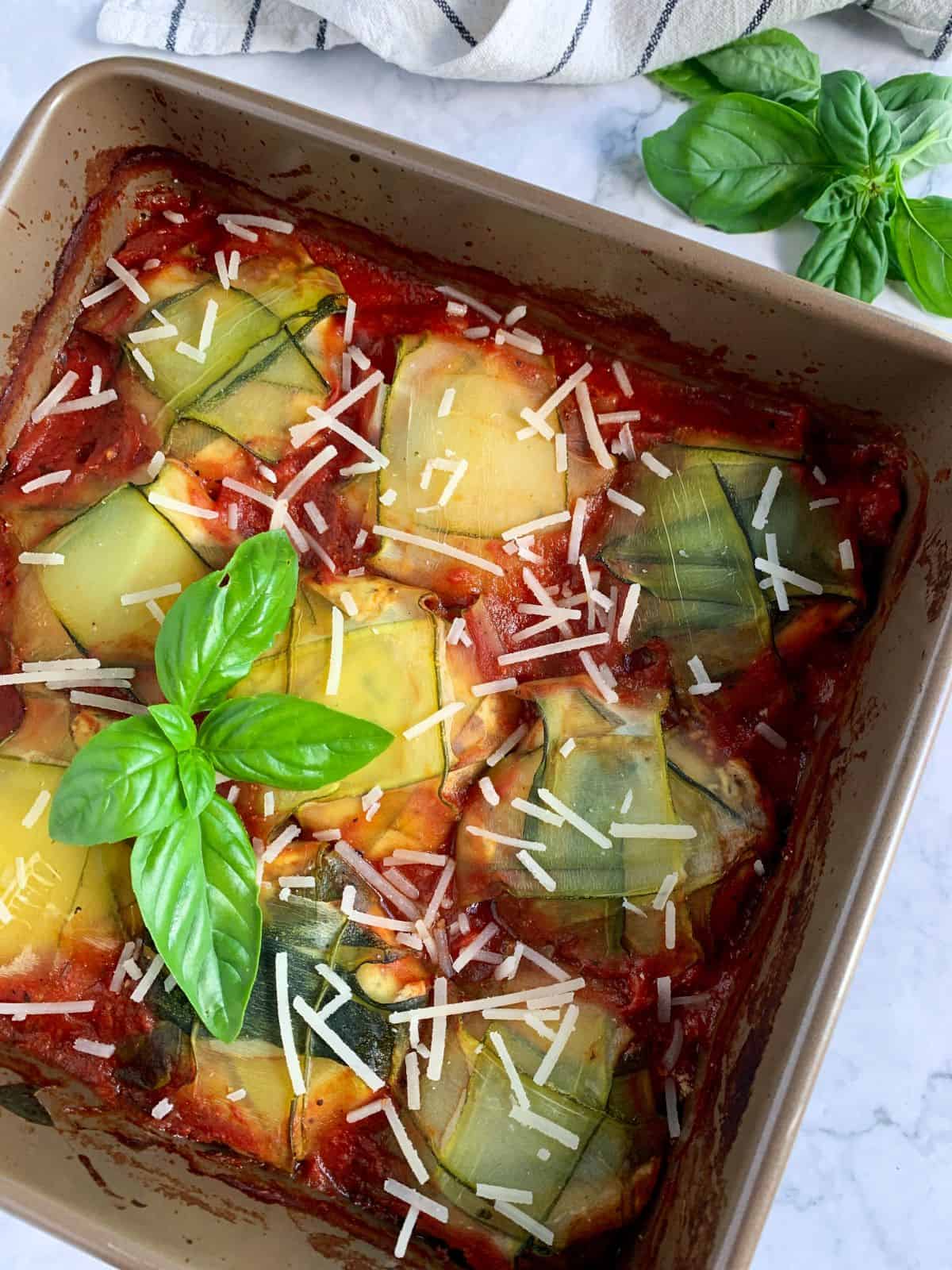 zucchini ravioli in a baking dish with basil and vegan parmesan
