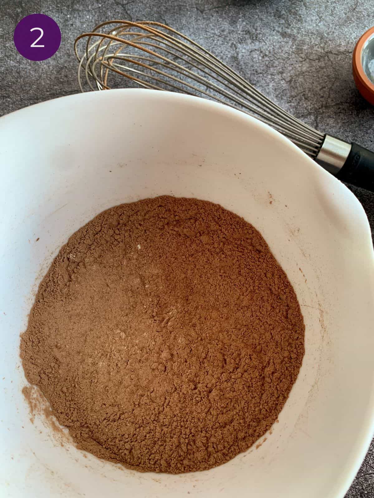 Dry ingredients whisked together in a white bowl with metal whisk.