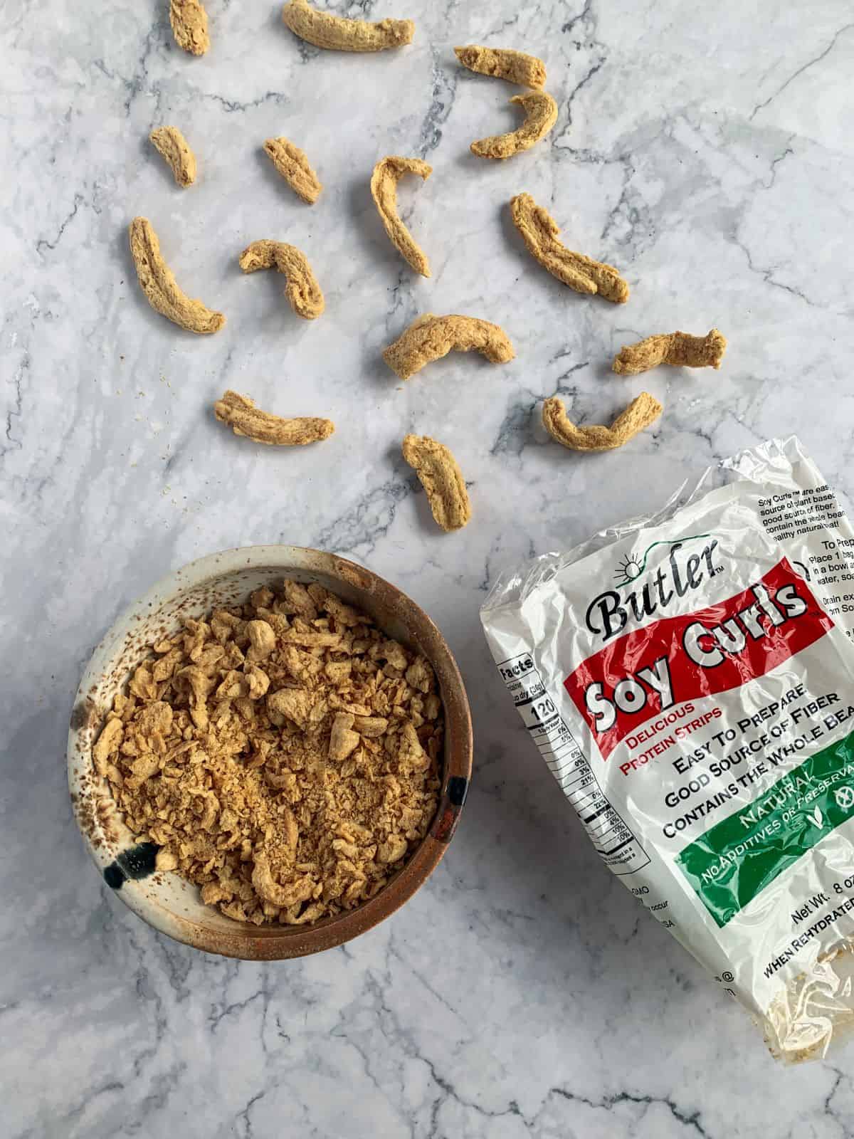 Soy curls whole and crumbled on a white surface with a Butler's Soy Curl bag.