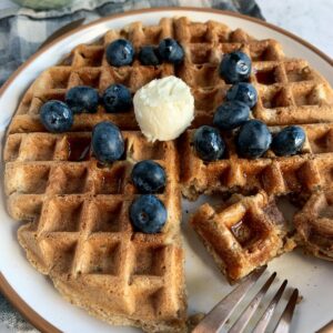 Vegan oatmeal waffles with blueberries, butter and syrup on a plate.