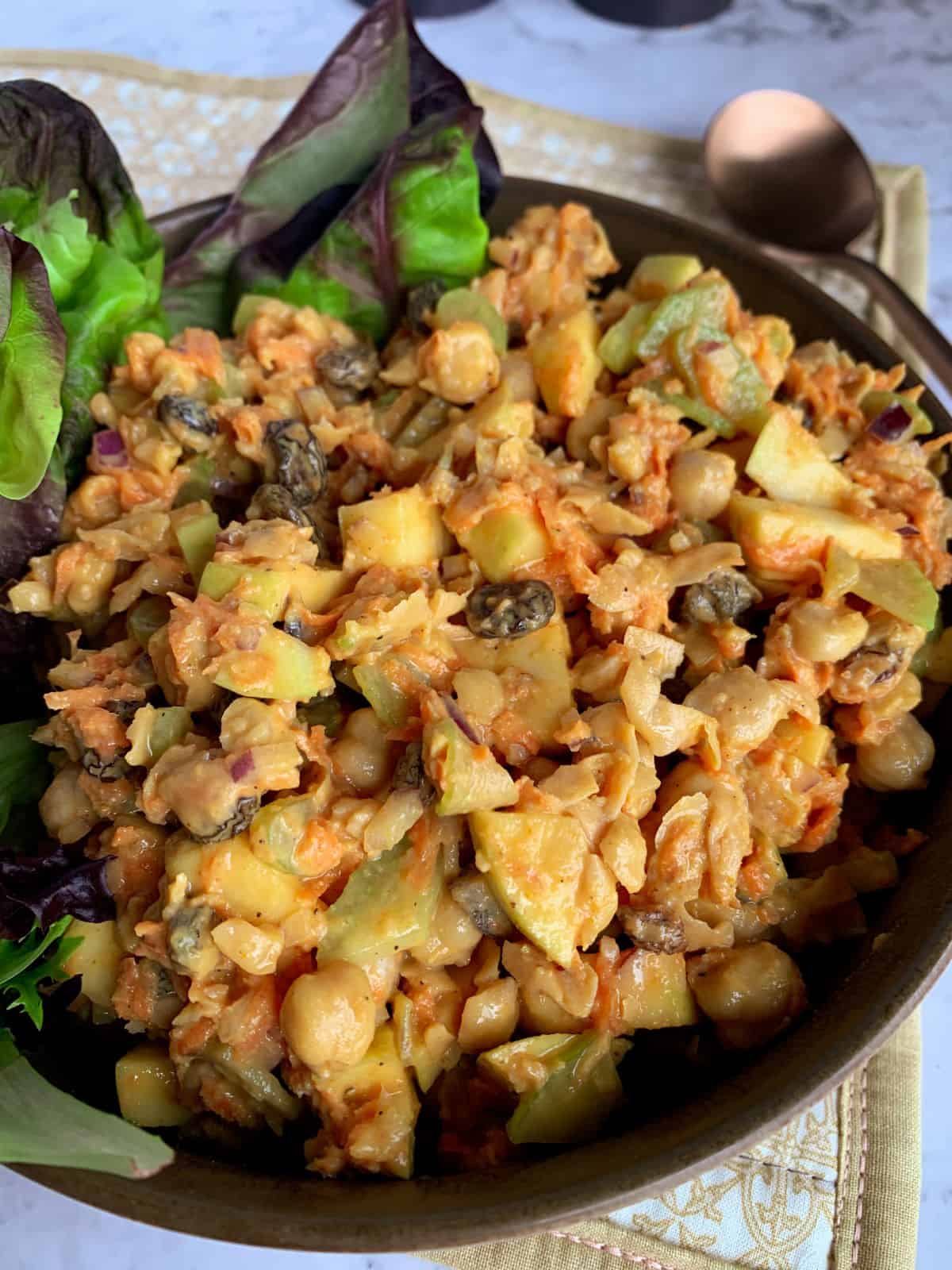 Prepared curry chickpea salad with greens in a brown bowl.