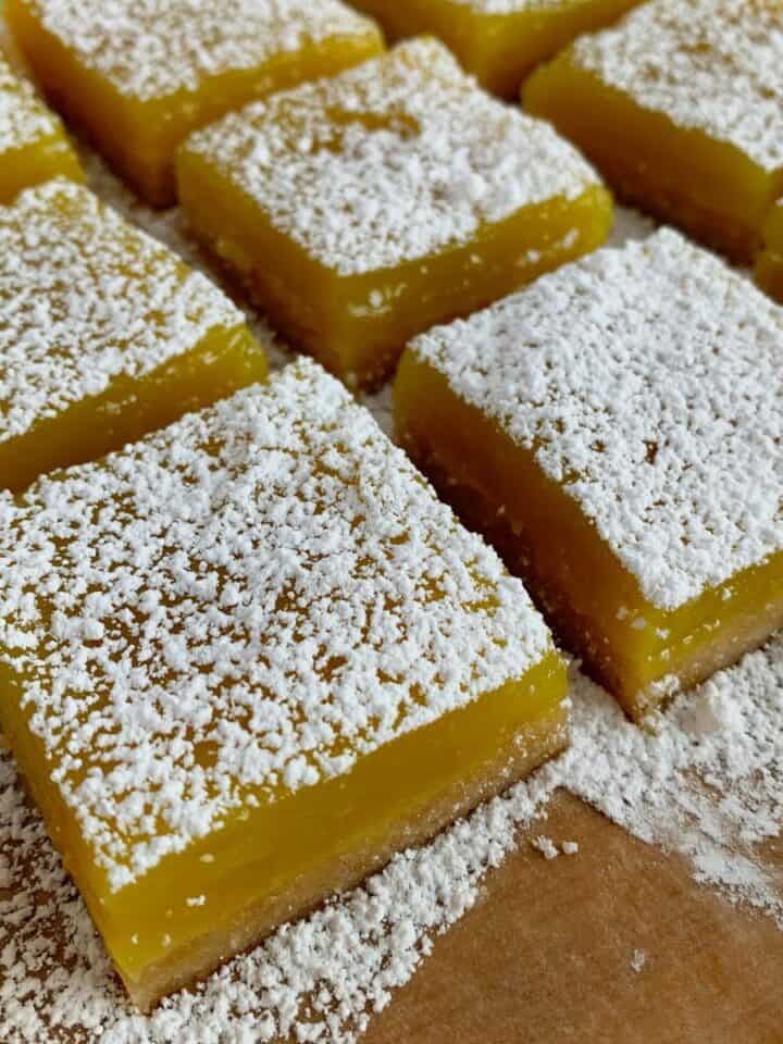 Vegan, no-bake lemon bars sliced and topped with powdered sugar.