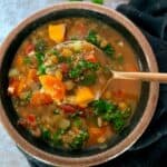 Lentil quinoa soup with vegetables in a bowl with a bite on a gold spoon.
