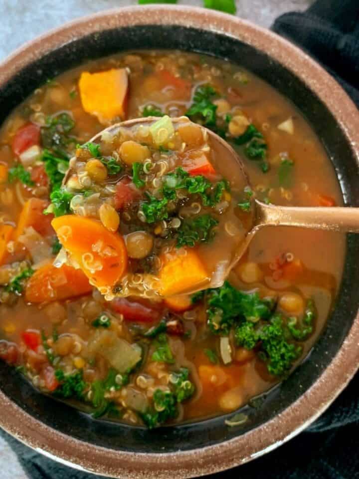 Lentil quinoa soup with vegetables in a bowl with a bite on a gold spoon.