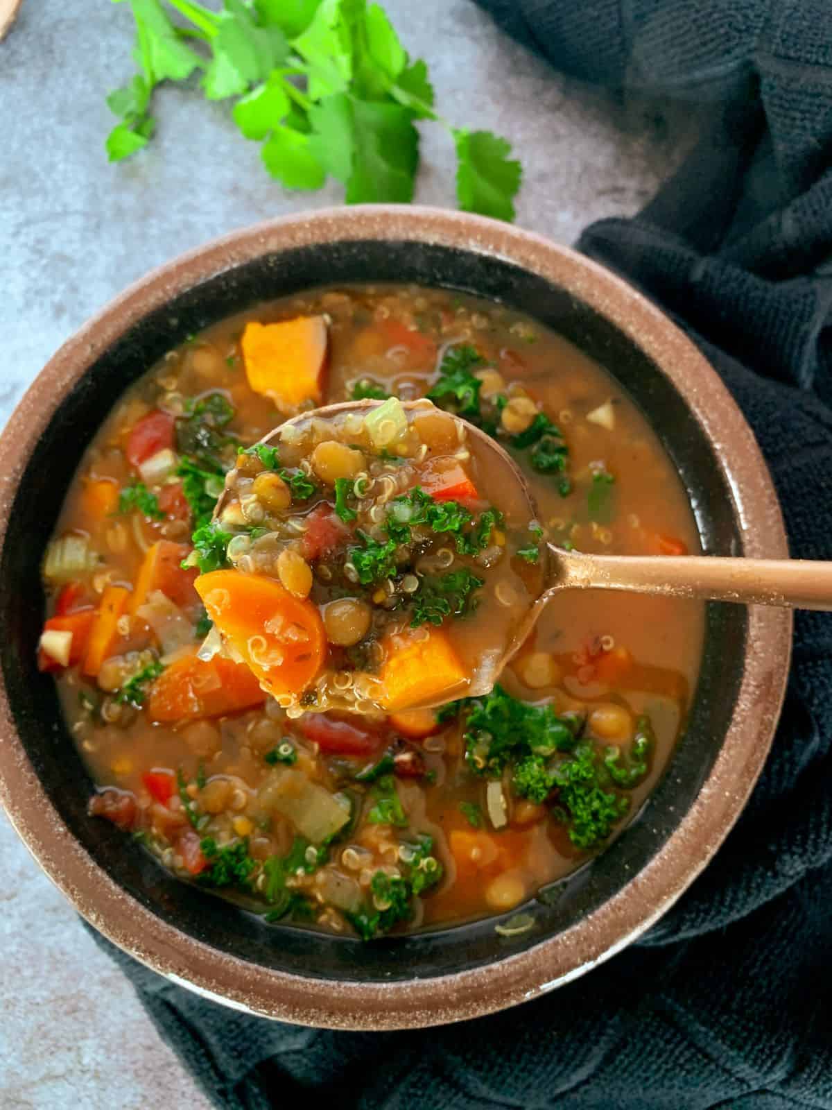 Lentil Quinoa soup in a bowl with a bite on a spoon. Soup is full of kale, peppers, sweet potatoes and more.