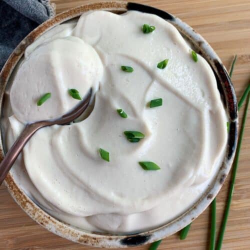 Vegan Sour Cream made with silken tofu and topped with chives in a bowl with a spoon.