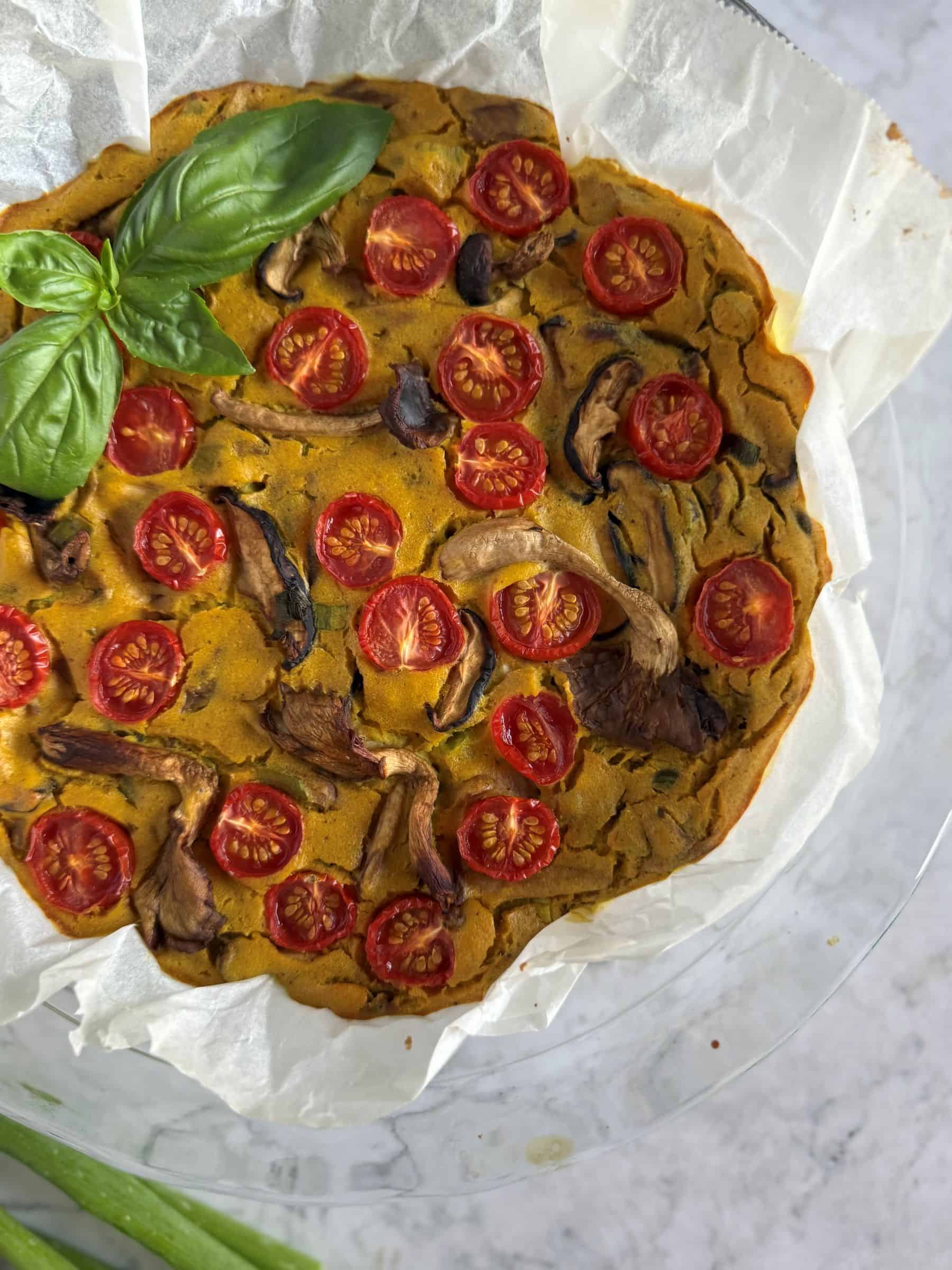 Vegan frittata with mushrooms and tomatoes in a pie dish with parchment paper.