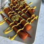 Vegan smoky carrot dogs on a plate with mustard and relish.