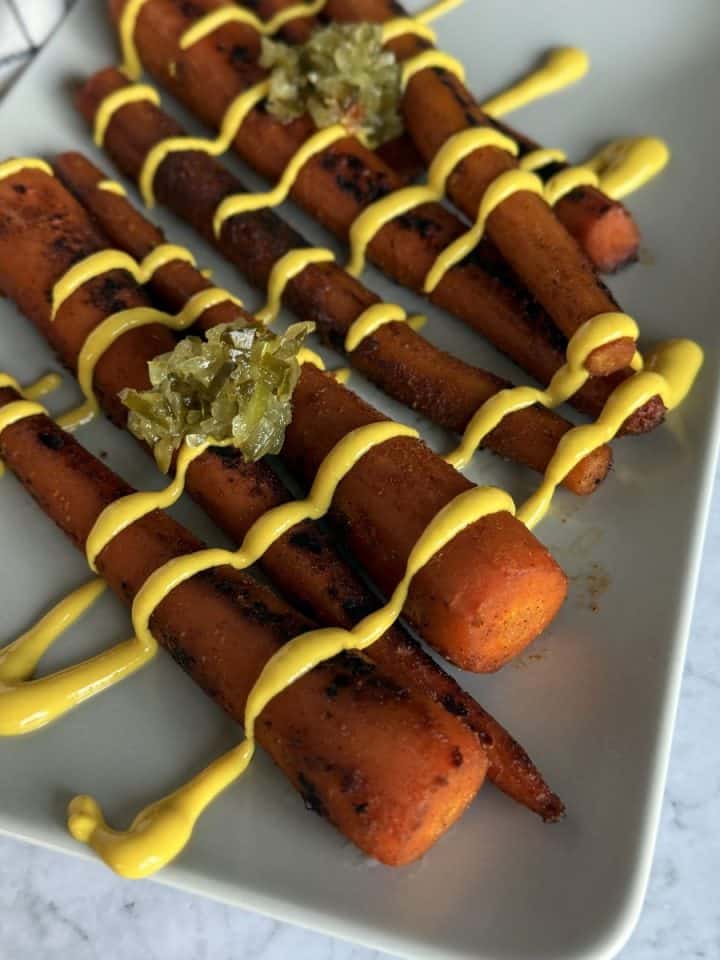 Vegan smoky carrot dogs on a plate with mustard and relish.